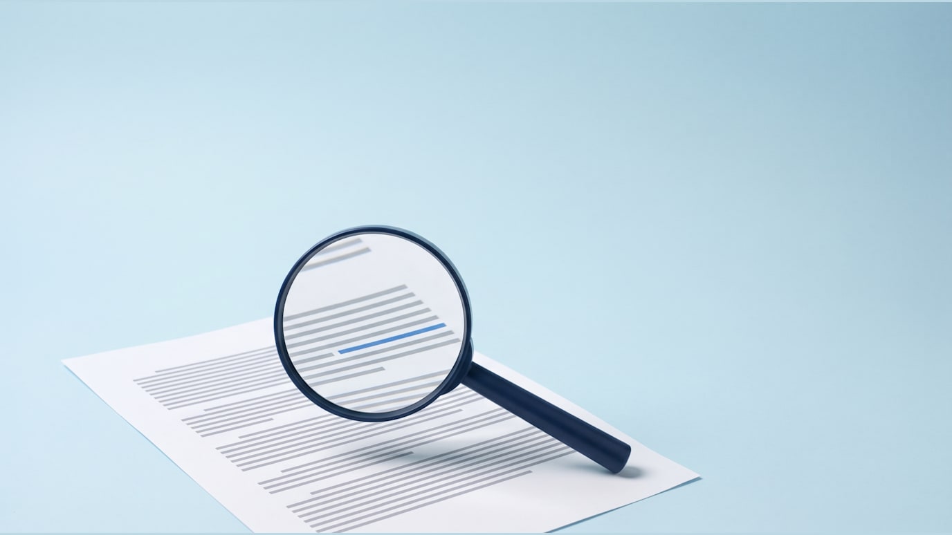 A navy magnifying glass hovering over a printed white page of grey lines