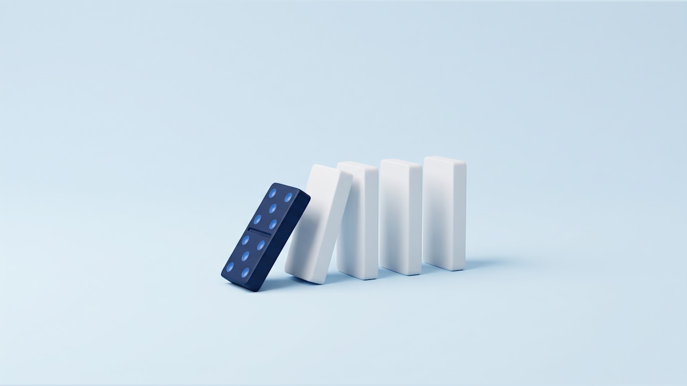 A single navy domino tipping forward to start a short row of standing white dominoes