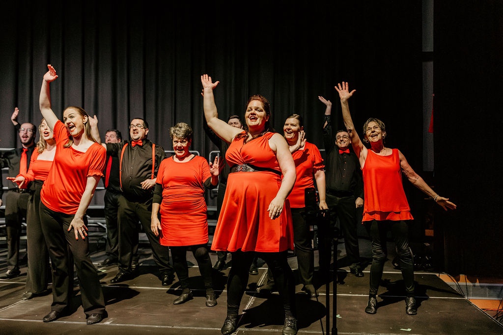 Joyful musical theatre ensemble performing together on stage under warm lights